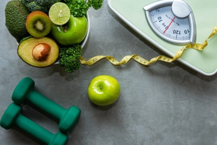 Weight loss and weight gain program essentials – fresh green vegetables, weighing scale, measuring tape and dumbbells for balance diet coaching